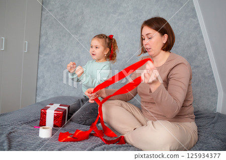Mid shot of adult mother and her daughter pack a gift together for Valentine's Day and Mother's Day. Caucasian woman and a cute little girl spend time together 125934377
