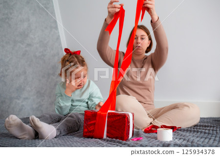 Bottom view of young mother and her daughter pack a gift together for Valentine's Day and Mother's Day. Caucasian woman and a cute little girl spend time together 125934378