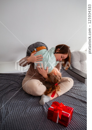 Happy of young Caucasian woman hugs and play with her daughter. Girl prepared a gift for her mother for the holiday. Concept of family time. Vertical orientation 125934383