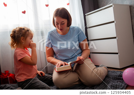 Caucasian teacher is reading book to a little girl, sitting on the floor. The concept of preschool education for children and Mother's Day 125934405