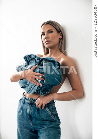 Model poses with denim clothing in a minimalist indoor setting during a fashion shoot 125934507