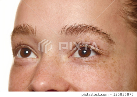 Side close-up a young woman eyes and eyebrow, showcasing natural skin with freckles isolated over white background. Side close-up a young woman eyes and eyebrow, showcasing natural skin with freckles isolated over white background. 125935975