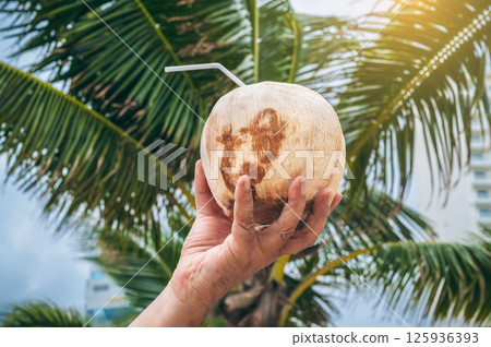 drinking coconut with a straw in a man's hand on background of palm trees. Concept of traveling and relaxing in a tropical resort on a sunny day 125936393