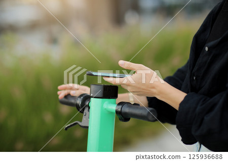 Cropped photo of woman with smartphone scans QR code for electric scooter rental. Girl using app on phone to unlock dockless transport outdoors. Urban riding ecological vehicle. Modern technology 125936688