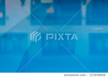 Close up out of focus bright blue water of indoor swimming pool with houseplants and large panoramic windows, lighting. Interior part of luxury modern wellness spa hotel. Healthy concept. Close up out of focus bright blue water of indoor swimming pool with houseplants and large panoramic windows, lighting. Interior part of luxury modern wellness spa hotel. Healthy concept. 125936689