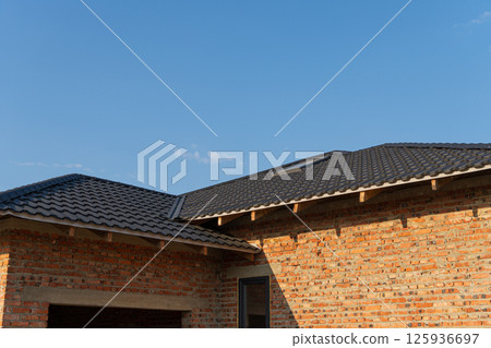A newly finished brick house features a sleek black tiled roof under a clear sunset sky with scattered clouds, highlighting modern architecture A newly finished brick house features a sleek black tiled roof under a clear sunset sky with scattered clouds, highlighting modern architecture 125936697
