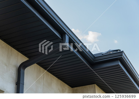 Exterior view of a contemporary home highlighting a sleek black gutter along the roofline under a bright blue sky 125936699