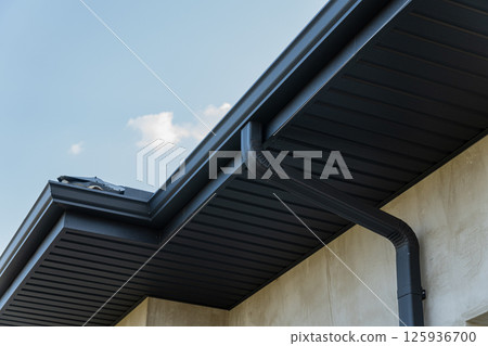 Close view of a roof edge and downspout against a bright blue sky highlights contemporary construction features and materials 125936700