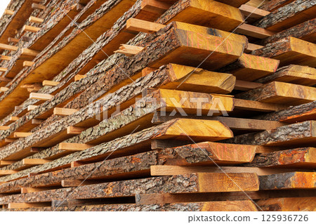 Wooden planks are neatly stacked and drying in the sunlight at a lumber yard, showcasing the natural textures and colors of the wood Wooden planks are neatly stacked and drying in the sunlight at a lumber yard, showcasing the natural textures and colors of the wood 125936726
