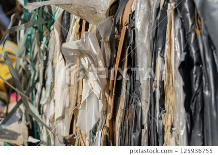 Large bales of compressed plastic waste sit tightly packed at a recycling facility under clear blue skies, reflecting sustainability efforts 125936755
