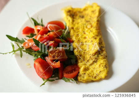 Healthy breakfast with omelette and fresh salad with cherry tomatoes and arugula, dressed with mustard, honey and olive oil sauce on white plate. Nutritious meal with protein and fiber. Ketogenic diet 125936845
