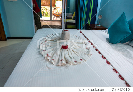 Hotel bed with towel swans, flowers, and blue pillows in a cozy room 125937010