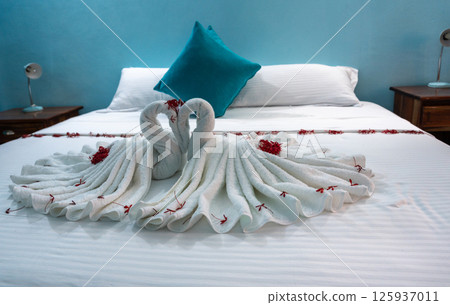 Hotel bed with towel swans, flowers, and blue pillows in a cozy room Hotel bed with towel swans, flowers, and blue pillows in a cozy room 125937011