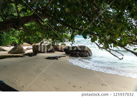 Shaded tropical beach on Seychelles island with white sand, granite boulders, calm waves 125937032