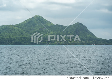 Mahe island in Seychelles, lush green hills and sandy beach seen across calm ocean Mahe island in Seychelles, lush green hills and sandy beach seen across calm ocean 125937036