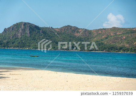 Praslin island in Seychelles, tropical beach with turquoise sea, forested hills and fishing boat Praslin island in Seychelles, tropical beach with turquoise sea, forested hills and fishing boat 125937039