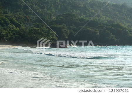 Close-up texture of ocean waves and sandy beach under sunlight with turquoise tones and soft foam 125937061