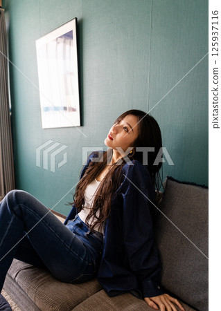 Beautiful Japanese woman in denim sitting on a sofa 125937116