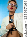 Sexy, liberated LGBT girl with glasses, short hair and a white jacket on her naked body, posing erotically with a setoscope 125937164