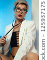 Sexy, liberated LGBT girl with glasses, short hair and a white jacket on her naked body, posing erotically with a setoscope 125937175