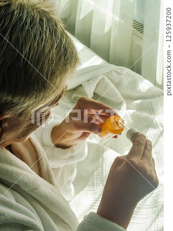 Woman in white robe applies serum in bright room with soft textures. High quality photo Woman in white robe applies serum in bright room with soft textures. High quality photo 125937200