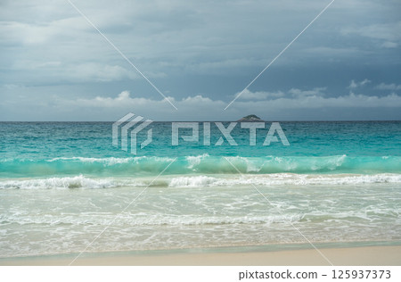 Tropical turquoise ocean waves breaking on sandy beach in Seychelles with distant island on horizon 125937373