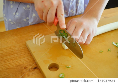 A fifth grade elementary school student is cutting onions with a knife 125937684