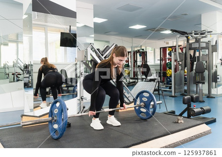 Young woman preparing to lift barbell in gym. Young woman preparing to lift barbell in gym. 125937861