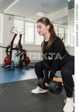 Woman lifting heavy dumbbell in squat position indoors. Woman lifting heavy dumbbell in squat position indoors. 125937867