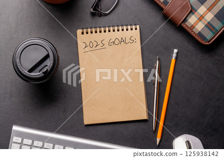 Elegant leather desk setup with laptop, coffee, stationery, and a notepad labeled 2025 Goals 125938142