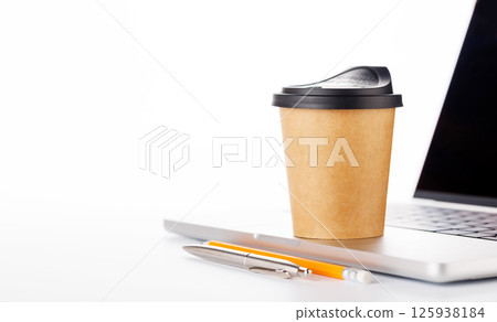 Closeup of an office table featuring a sleek laptop and a coffee cup on a clean white surface Closeup of an office table featuring a sleek laptop and a coffee cup on a clean white surface 125938184