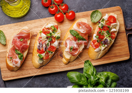 Tasty antipasto toasts featuring classic caprese with mozzarella and tomatoes, and savory prosciutto with herbs 125938199