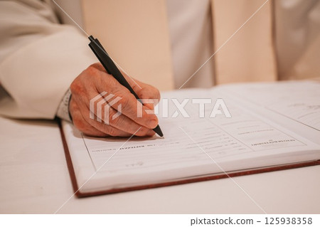 Priest Recording Baptism Details in Church Logbook 125938358