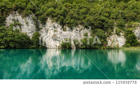 Turquoise lake reflecting lush green forest and white cliffs in plitvice lakes national park 125938778