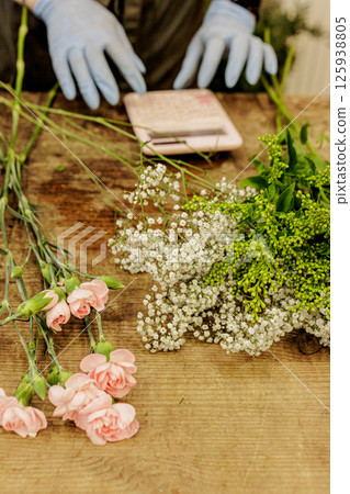 Florist arranging flowers with gypsophila and carnations on wooden table, mothers day 125938805