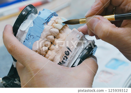 Dental Technician Carefully Brushes Denture Mold During Manufacturing Dental Technician Carefully Brushes Denture Mold During Manufacturing 125939312