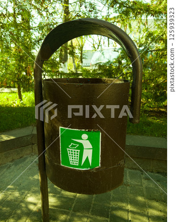 Unique outdoor trash bin with green recycling symbol in a serene park setting Unique outdoor trash bin with green recycling symbol in a serene park setting 125939323