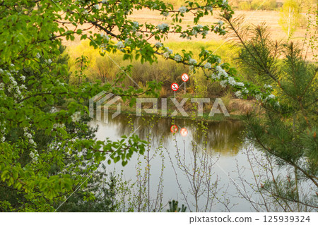 Tranquil riverside setting with warning signs and lush greenery in spring Tranquil riverside setting with warning signs and lush greenery in spring 125939324