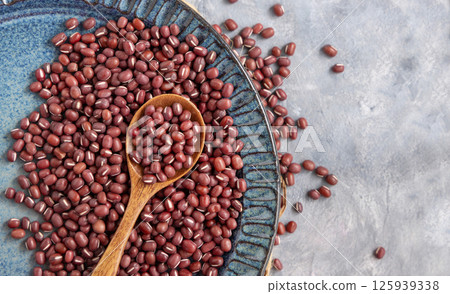 Blue plate full of dried red azuki beans with a wooden spoon top view. Vegetarian protein source Blue plate full of dried red azuki beans with a wooden spoon top view. Vegetarian protein source 125939338