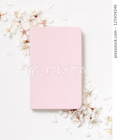 Light pink blank notebook near white cherry flowers top view, spring wedding mockup 125939340