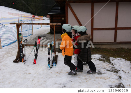 Young skiers prepare for their lessons at a snow covered mountain resort on a winter afternoon, excitedly gathering their equipment before hitting the slopes 125940929