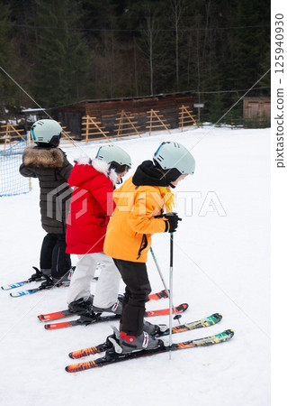 Excitement fills the air as young skiers take on the snowy slopes at a ski resort surrounded by tall trees and winter beauty 125940930