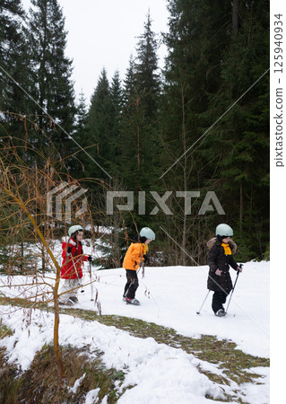 Children skiing through a snowy forest trail on a chilly winter afternoon, surrounded by tall evergreen trees and serene nature Children skiing through a snowy forest trail on a chilly winter afternoon, surrounded by tall evergreen trees and serene nature 125940934