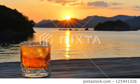 Refreshing drink with ice in whiskey glass against sunset over calm lake 125941326
