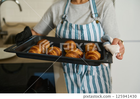 Woman Holding Baking Tray of Golden Freshly Baked Croissants in a Kitchen Woman Holding Baking Tray of Golden Freshly Baked Croissants in a Kitchen 125941430