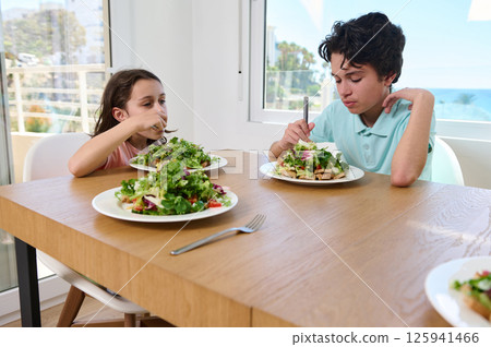 Children Eating Healthy Salad Together in a Bright Kitchen Children Eating Healthy Salad Together in a Bright Kitchen 125941466