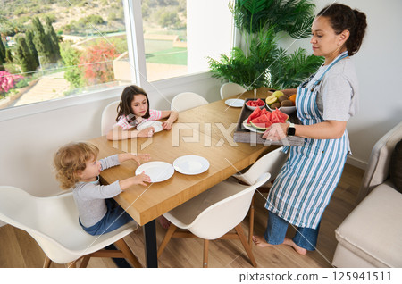 Mother Serving Healthy Breakfast to Children at Dining Table in Bright Home Mother Serving Healthy Breakfast to Children at Dining Table in Bright Home 125941511
