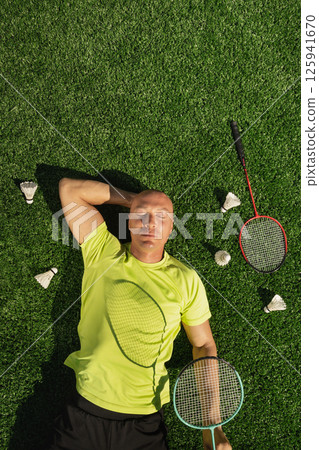 Badminton player resting after game, lying and enjoy on sport court in public park with artificial turf as green grass. Outdoors. Creative. Summer relax. View from above 125941670