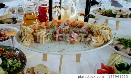 Gourmet appetizer spread featuring golden pancakes, delicate canapes, and assorted culinary delights arranged with artistic precision on elegant tabletop Gourmet appetizer spread featuring golden pancakes, delicate canapes, and assorted culinary delights arranged with artistic precision on elegant tabletop 125941923