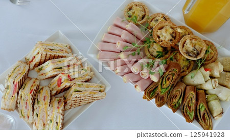 Club sandwiches, ham and cheese rolls, mini savory pies and crepes rolls served on a white table during a catered event, perfect for a business meeting or a special occasion 125941928
